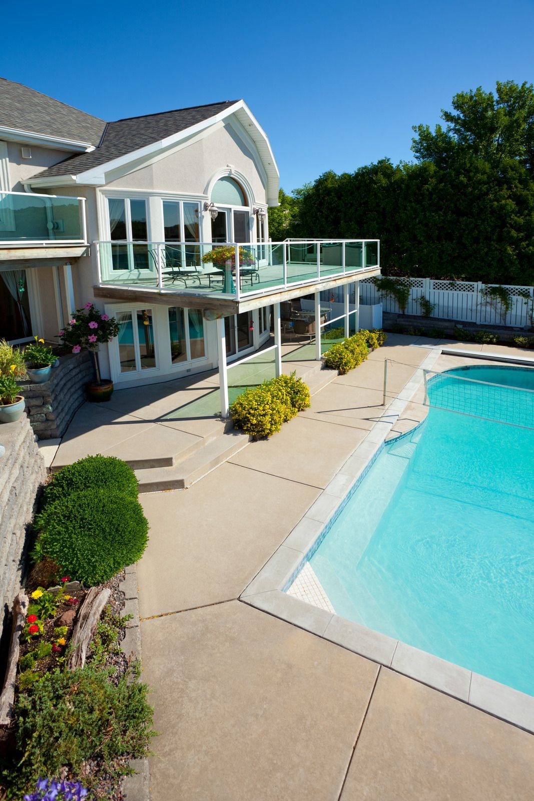 House with a pool, patio, and deck. Blue water, beige walls, clear deck railing, and lush green landscaping.