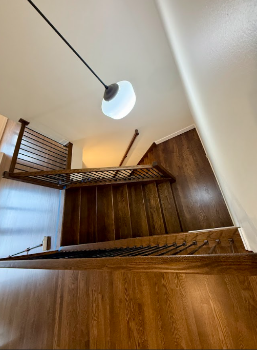 Looking down at a wooden staircase with a light hanging from the ceiling.