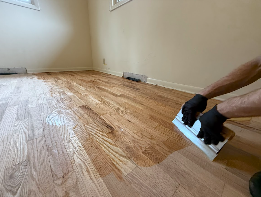A person is painting a wooden floor with a spatula.