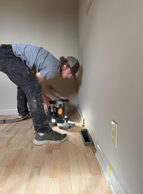 A man is working on a wooden floor in a room.