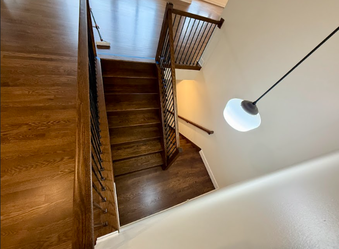A wooden staircase with a wrought iron railing and a light hanging from the ceiling.