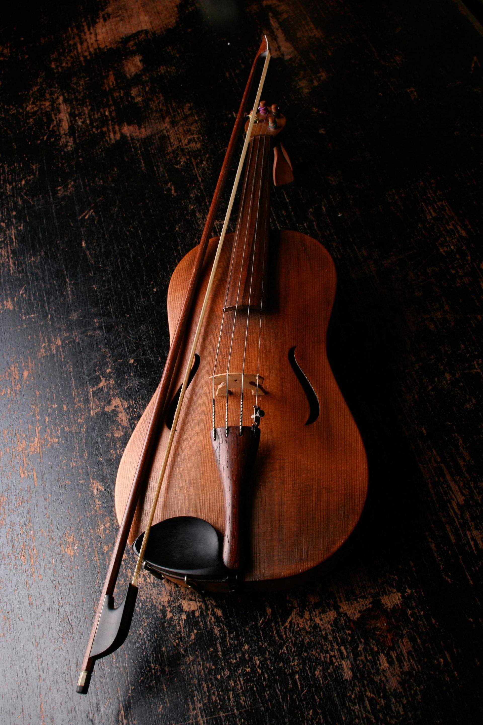 Wooden hurdy-gurdy with bow resting across the body, set against a dark textured surface.