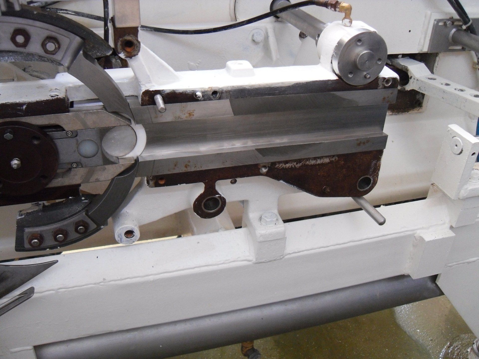 Macchina con componenti metallici, vernice bianca e una lama simile a una sega circolare, probabilmente per uso industriale.