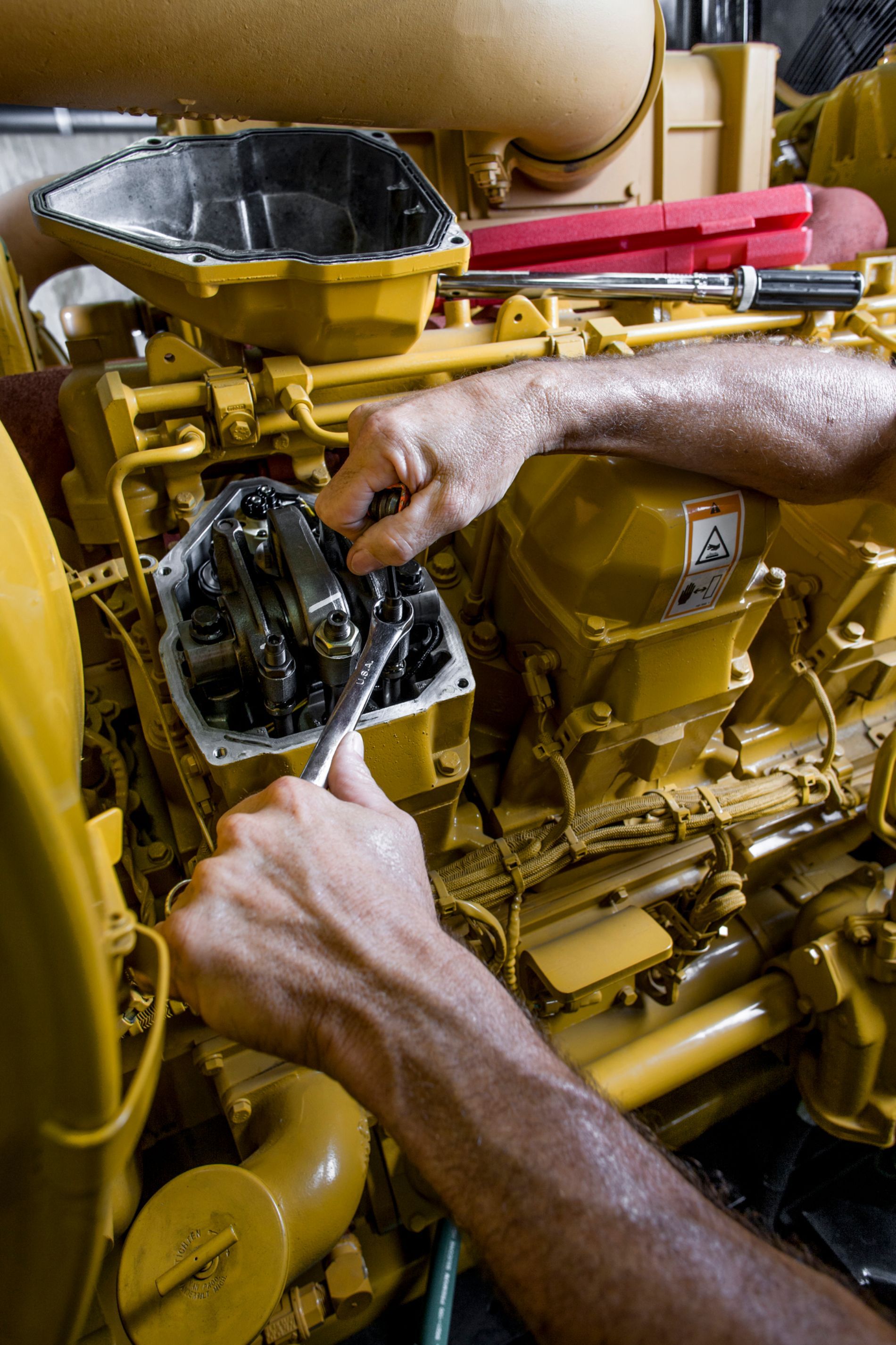 Meccanico al lavoro su un grande motore giallo con una chiave inglese. Il motore aperto mostra le parti interne.