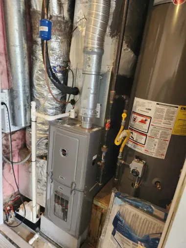 Basement furnace and HVAC equipment with metal ductwork, pipes, and a gray service panel