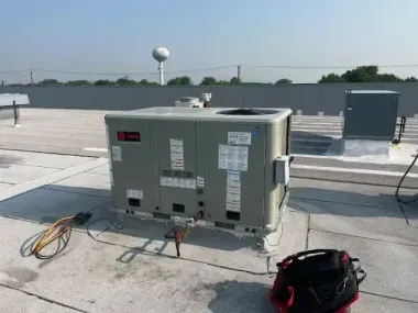 Large HVAC unit on a flat rooftop with cables and equipment nearby under a clear sky