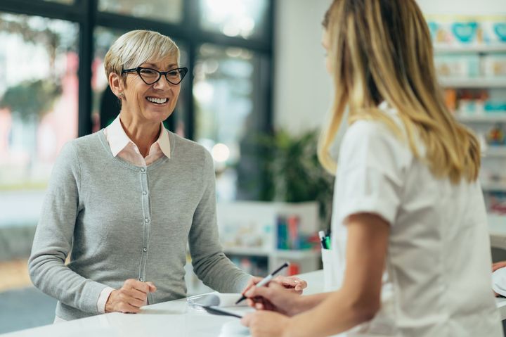 A woman is sitting at a counter in a pharmacy talking to a nurse.