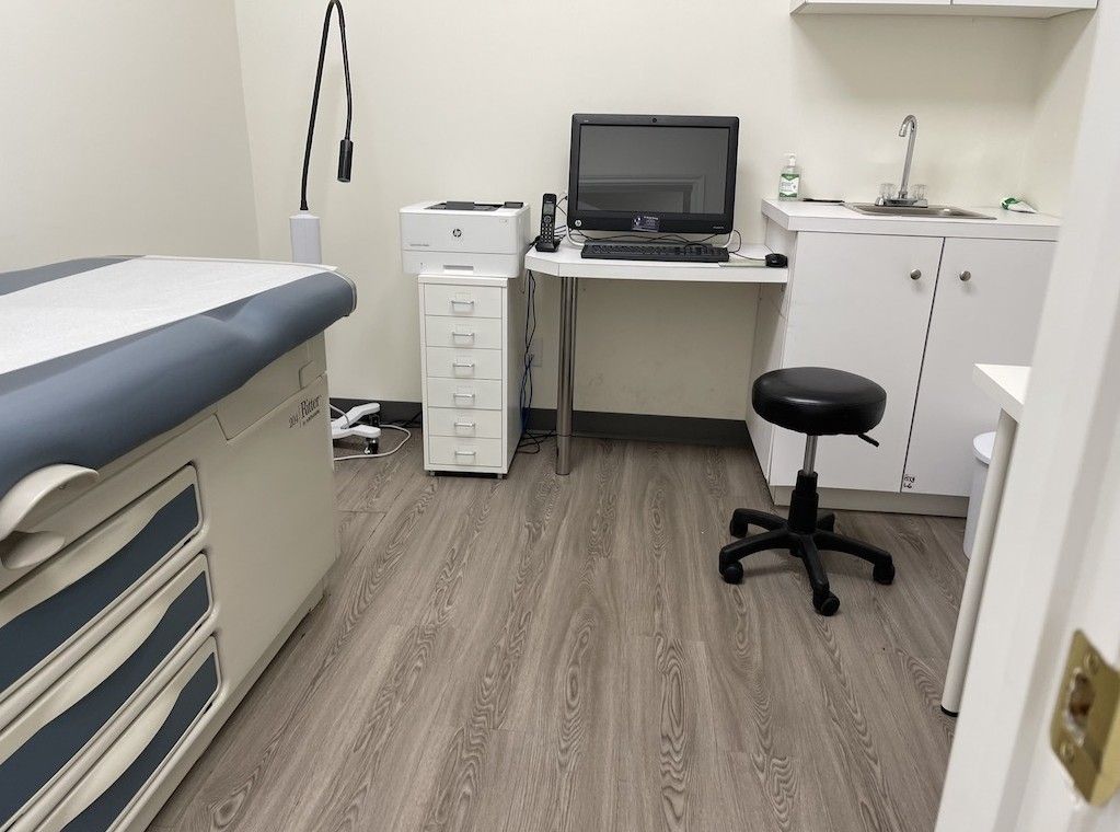 A doctor 's office with a stool , desk , computer and printer.