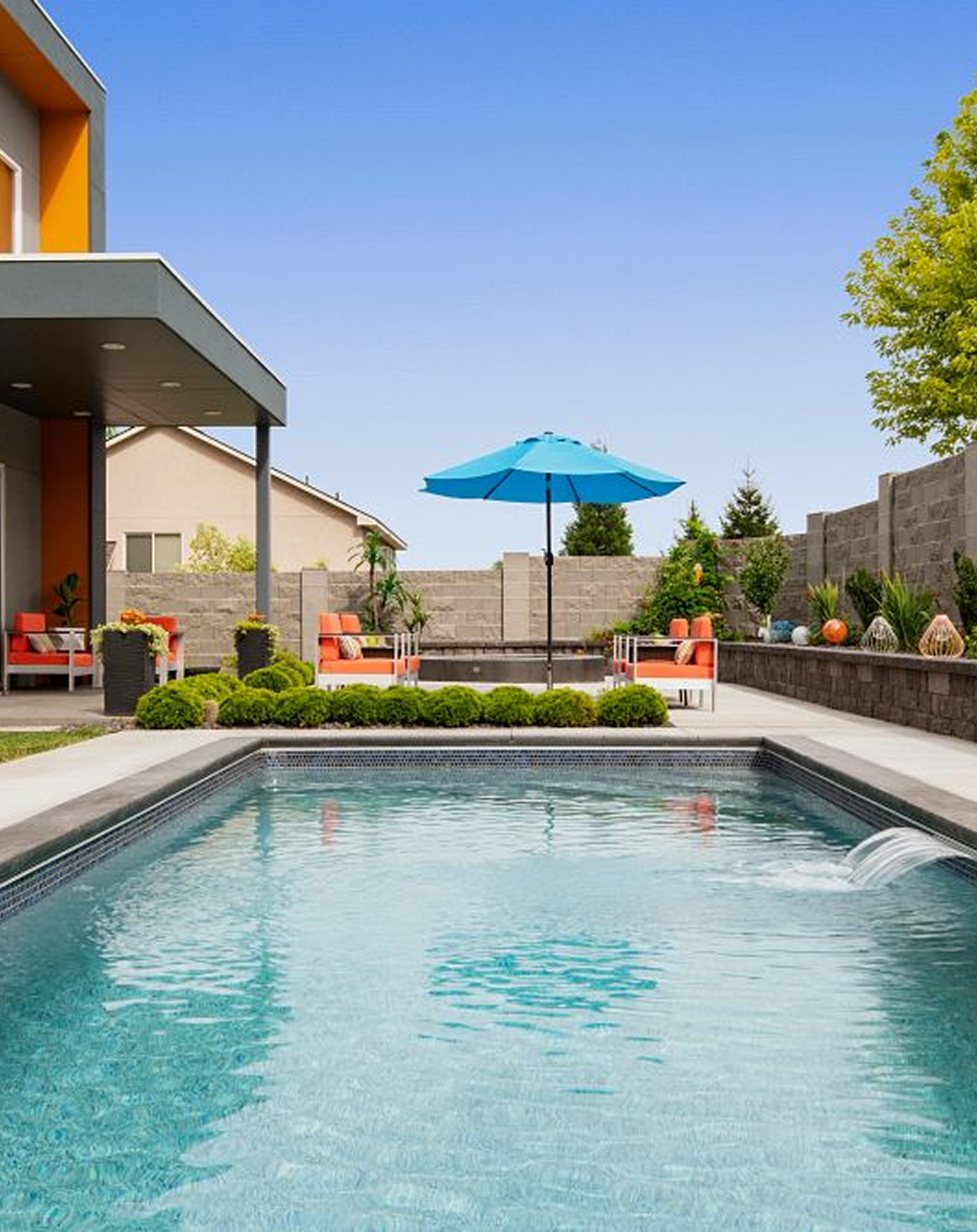 Swimming pool in a backyard with orange furniture, blue umbrella, and modern house.
