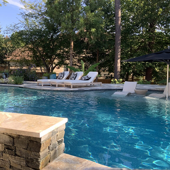 Swimming pool with lounge chairs, umbrella, and stone wall, surrounded by trees.