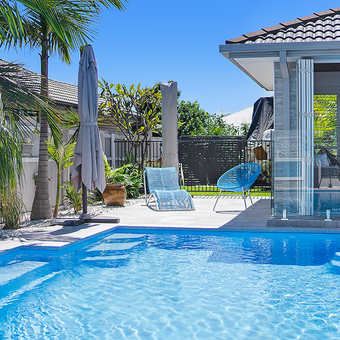 Swimming pool with blue water, outdoor seating, and a house on a sunny day.