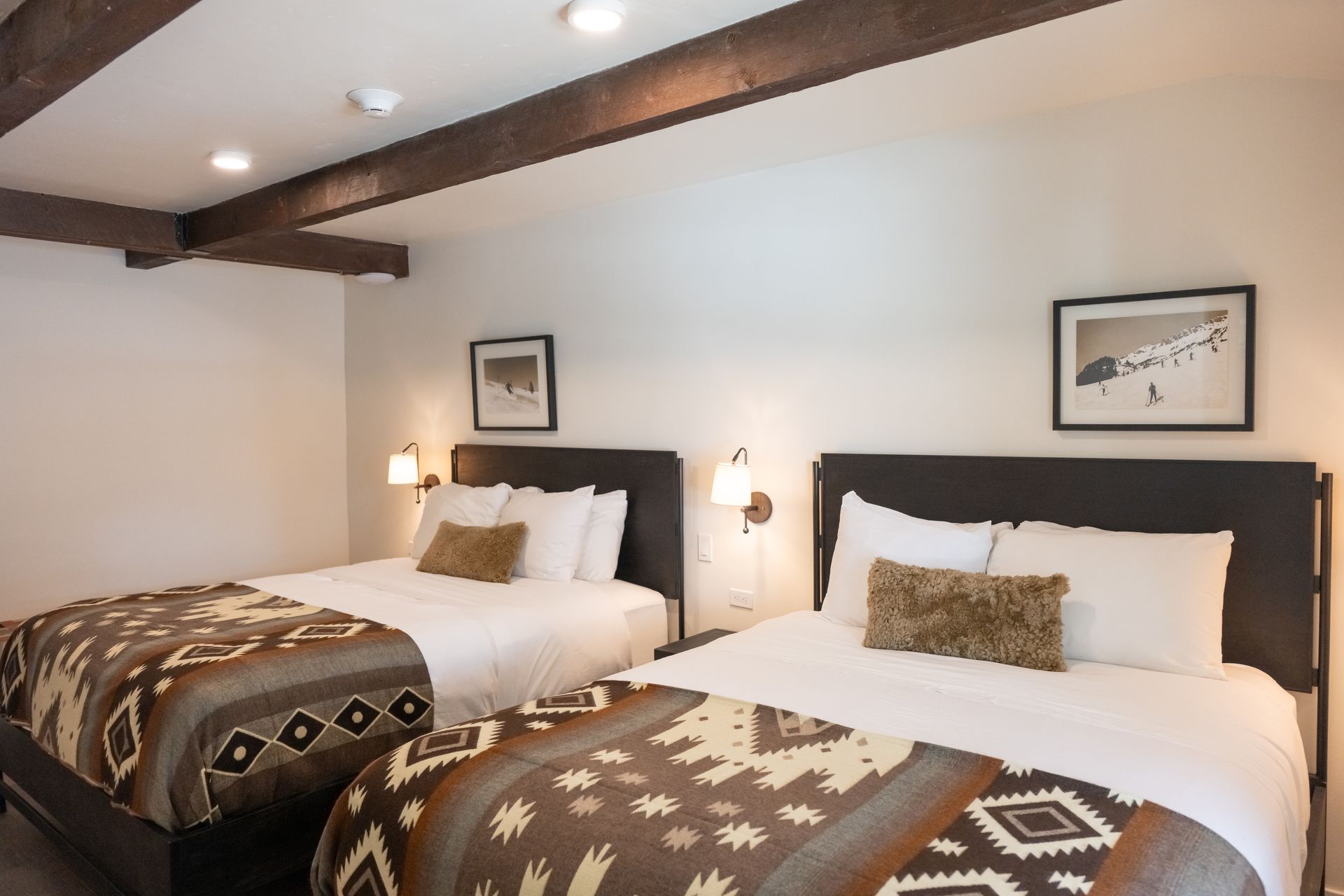 A hotel room with two queen beds, brown blankets, white bedding, and wall art.