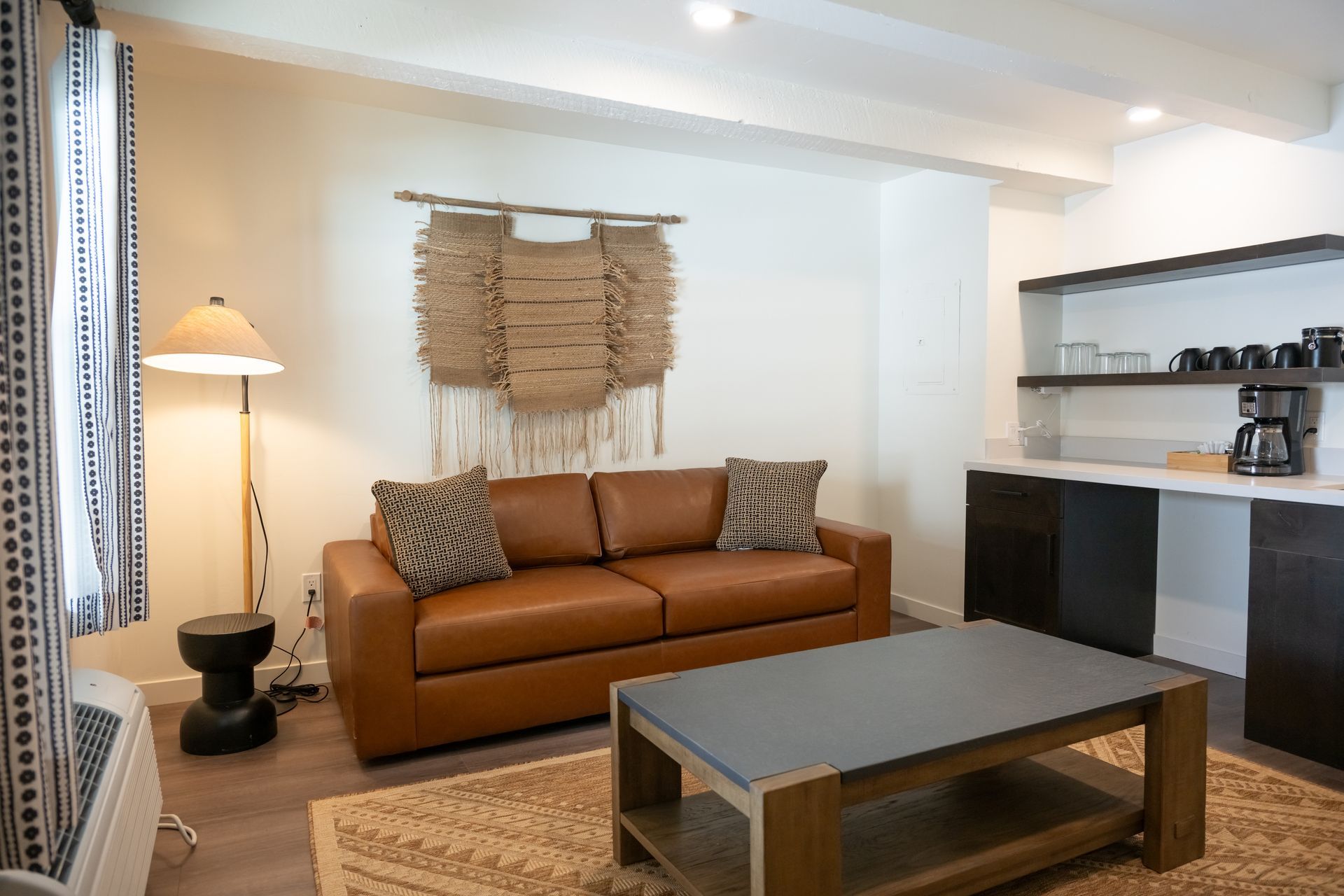 Cozy living room with brown leather sofa, rug, coffee table, and kitchenette.