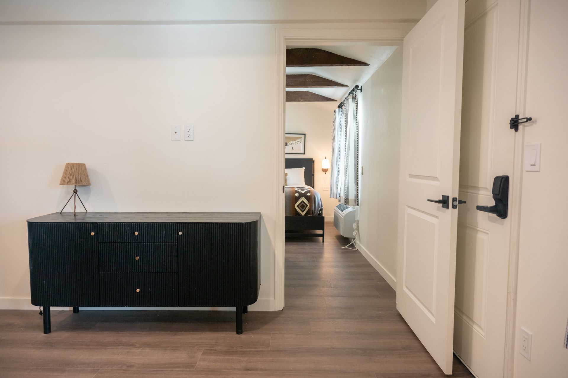 Hallway with a black cabinet, open door to a bedroom with a bed and curtained window.
