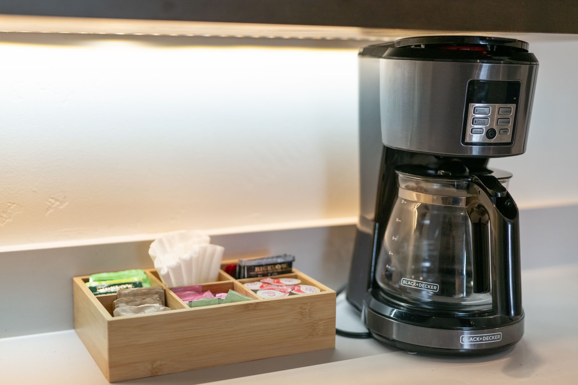 Coffee maker on counter next to a wooden box with tea, sugar, and coffee filters.