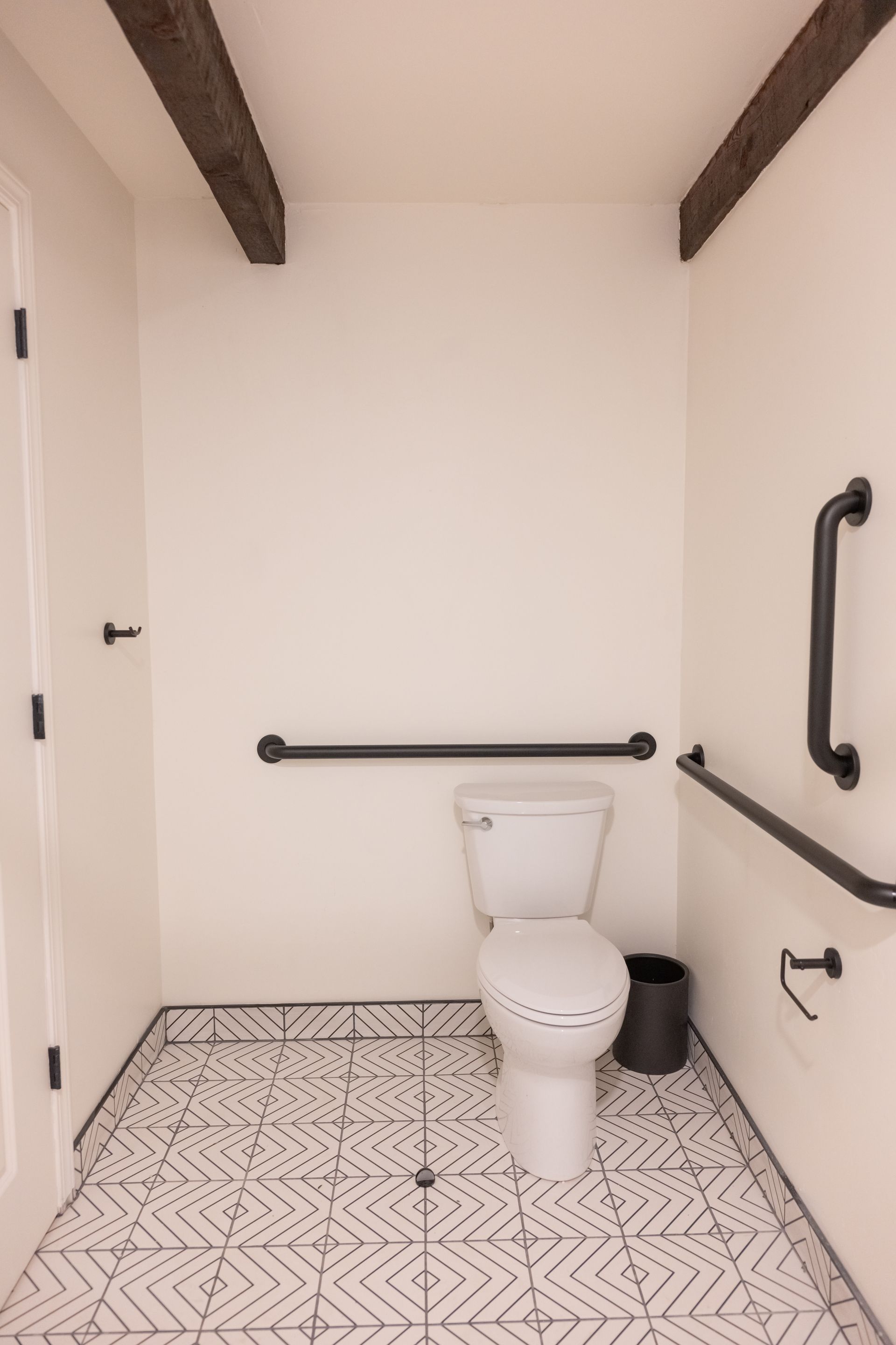 Accessible bathroom with toilet, grab bars, and patterned tile floor.