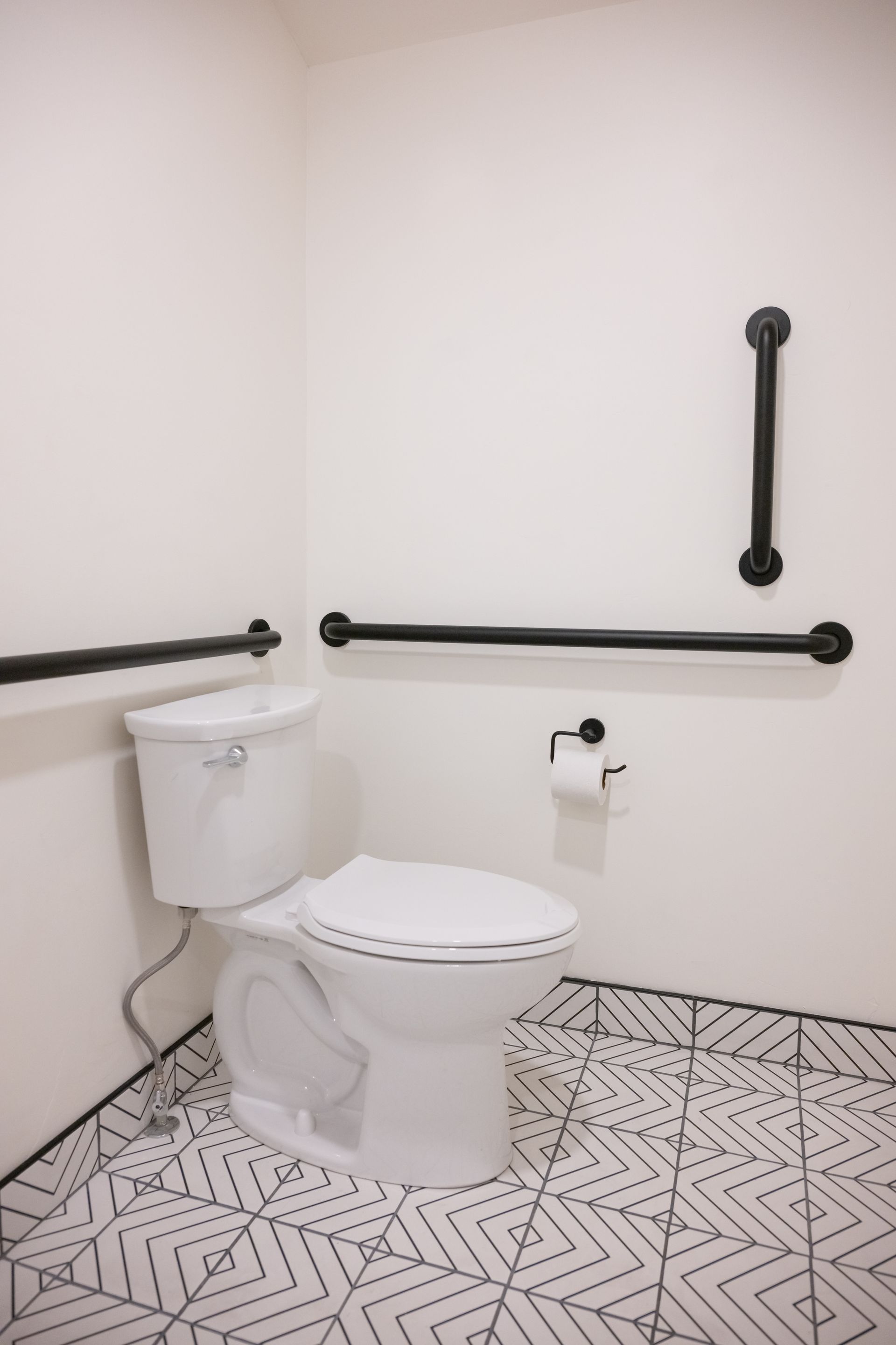 White accessible toilet with black grab bars in a corner, patterned floor.