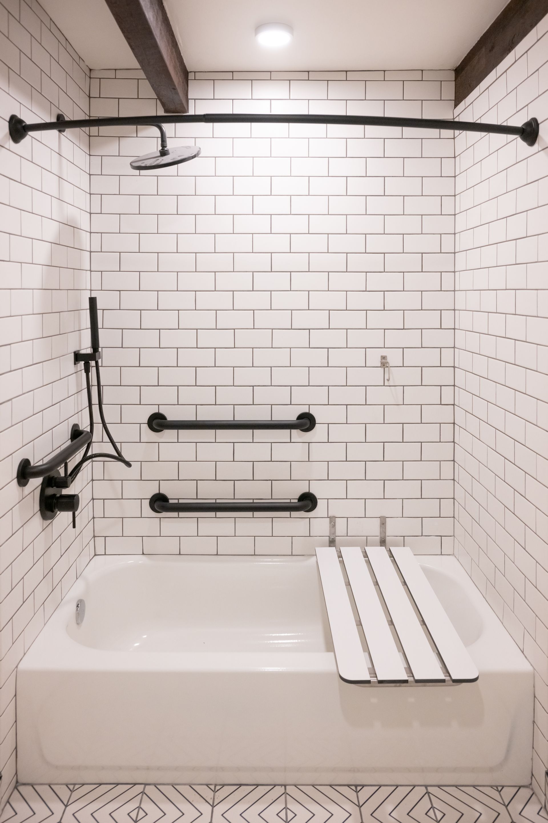 White tiled shower stall with grab bars, showerhead, and a seat.