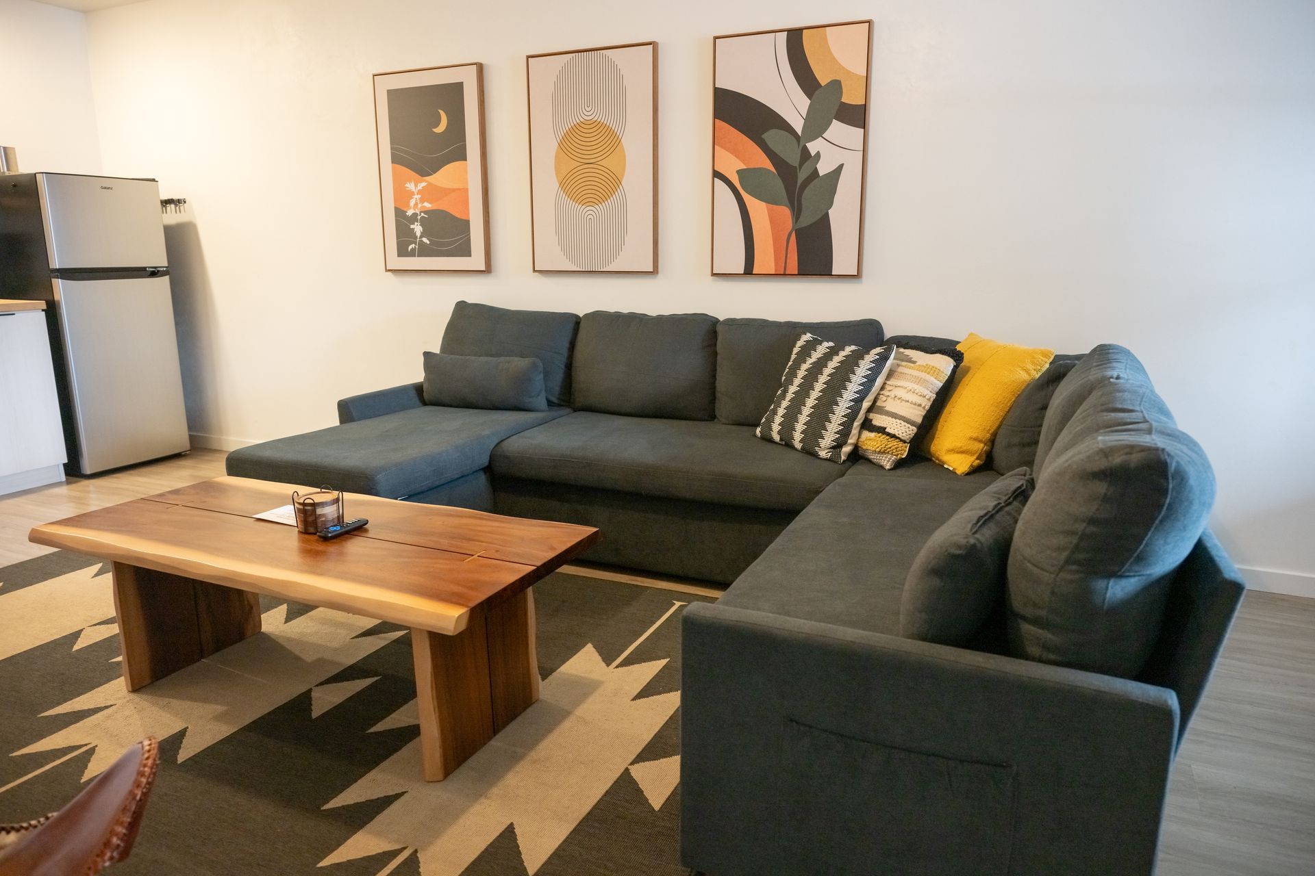 A modern living room with a gray sectional, wooden coffee table, and abstract wall art.