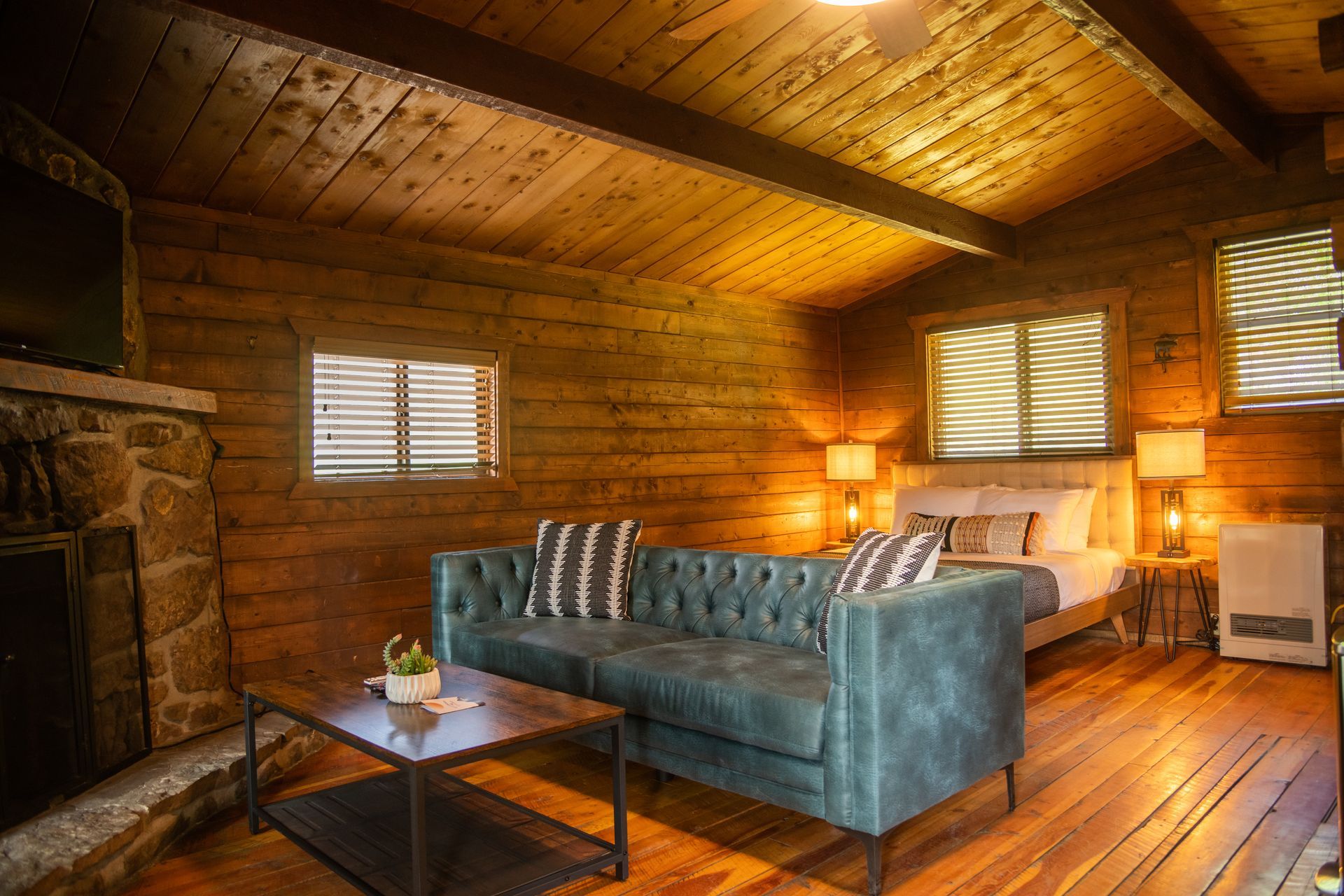 Cozy cabin interior with blue sofa, fireplace, bed, and wood paneling.