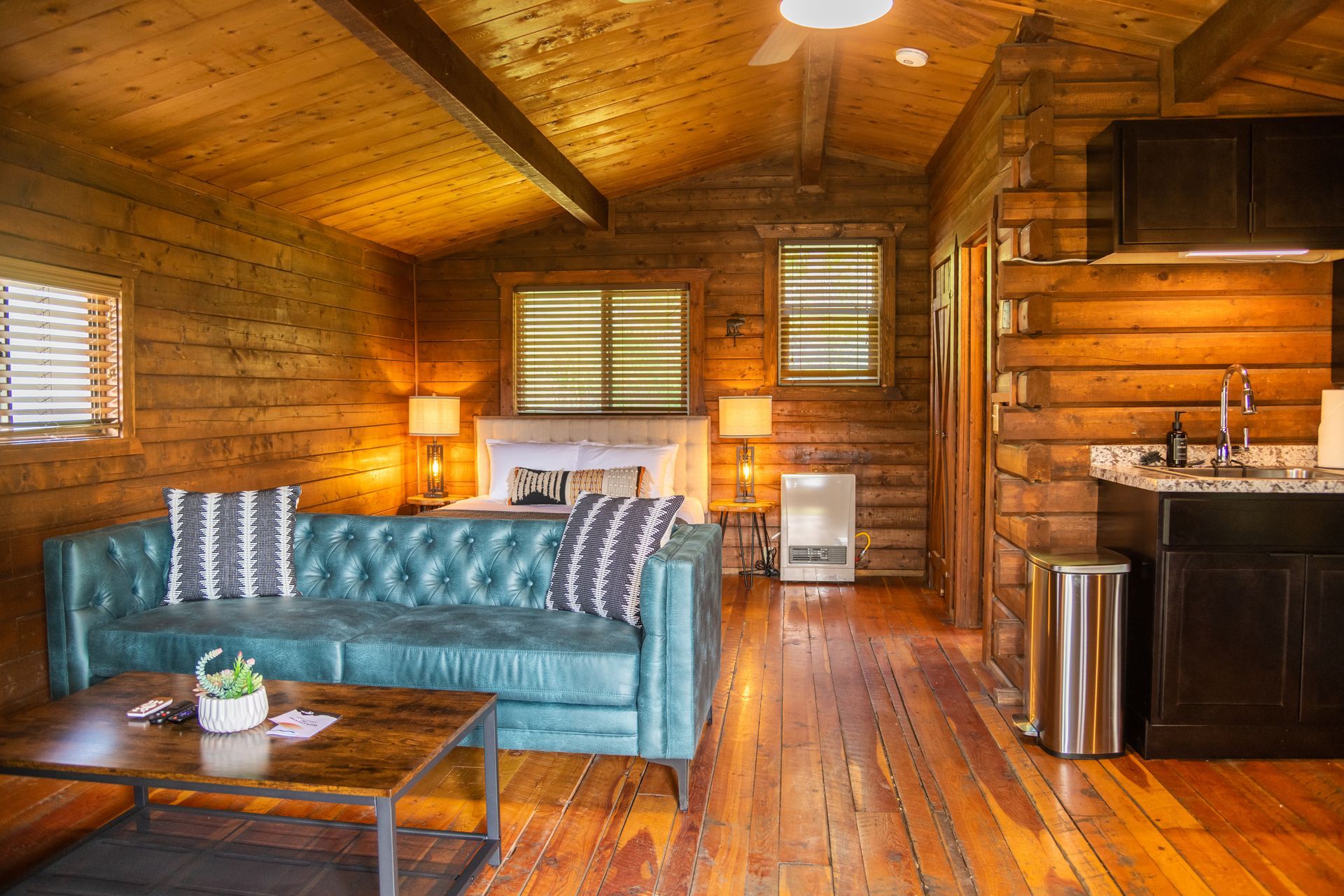 Cozy cabin interior with blue couch, wooden walls, and kitchen area.