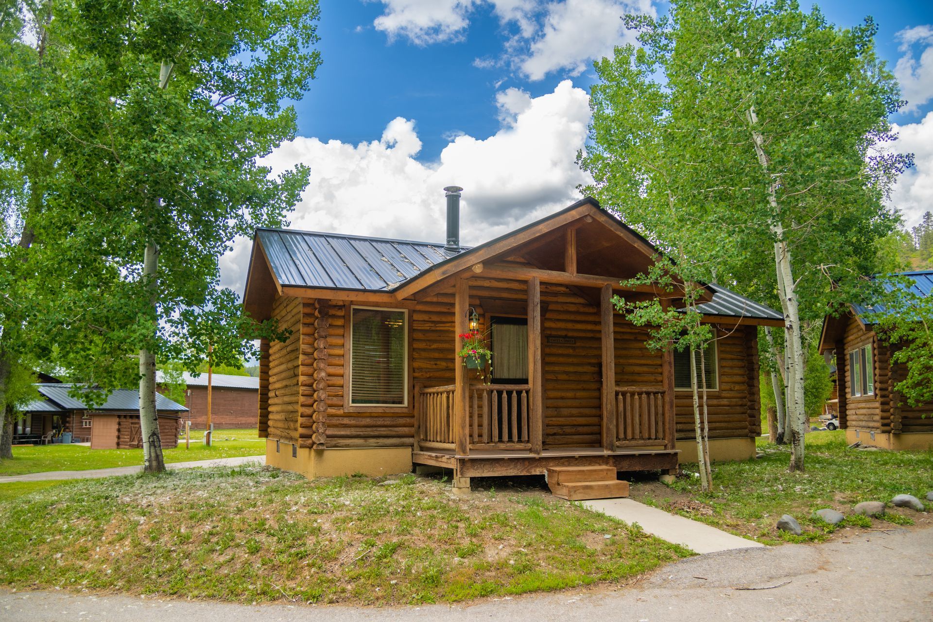 Log cabin with porch, trees, blue sky.