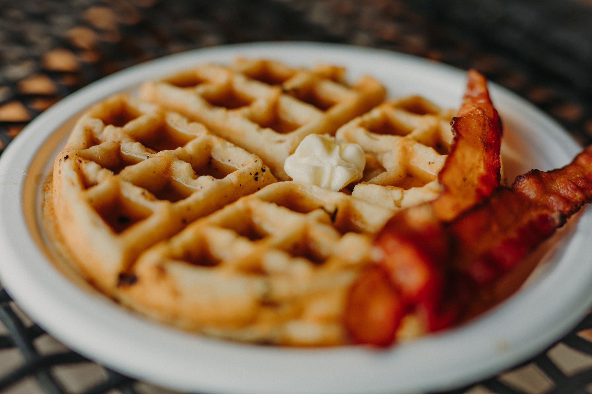 Waffle with butter and bacon on a white plate.