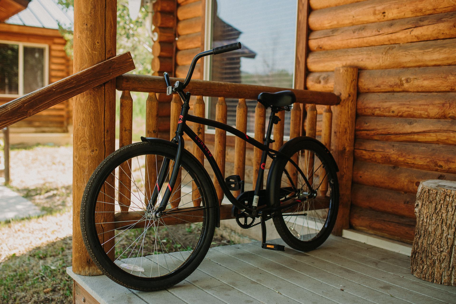 Black bicycle parked on a wooden porch of a log cabin.