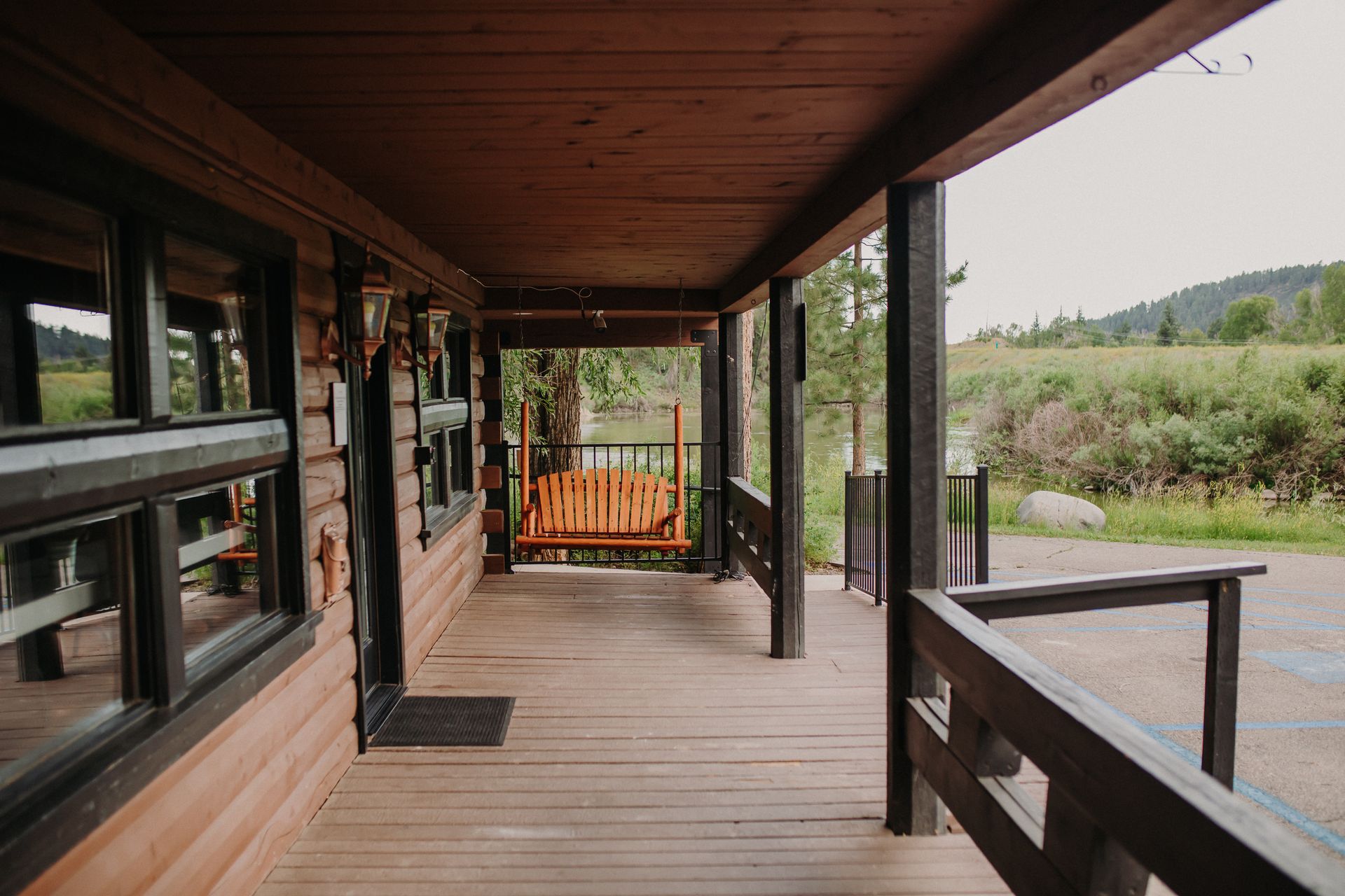 Wooden porch with a swing and view of a field, part of a log cabin.