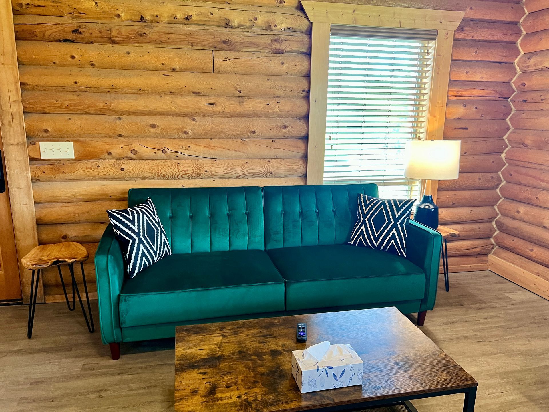 Green velvet sofa in a log cabin living room with coffee table and two patterned throw pillows.