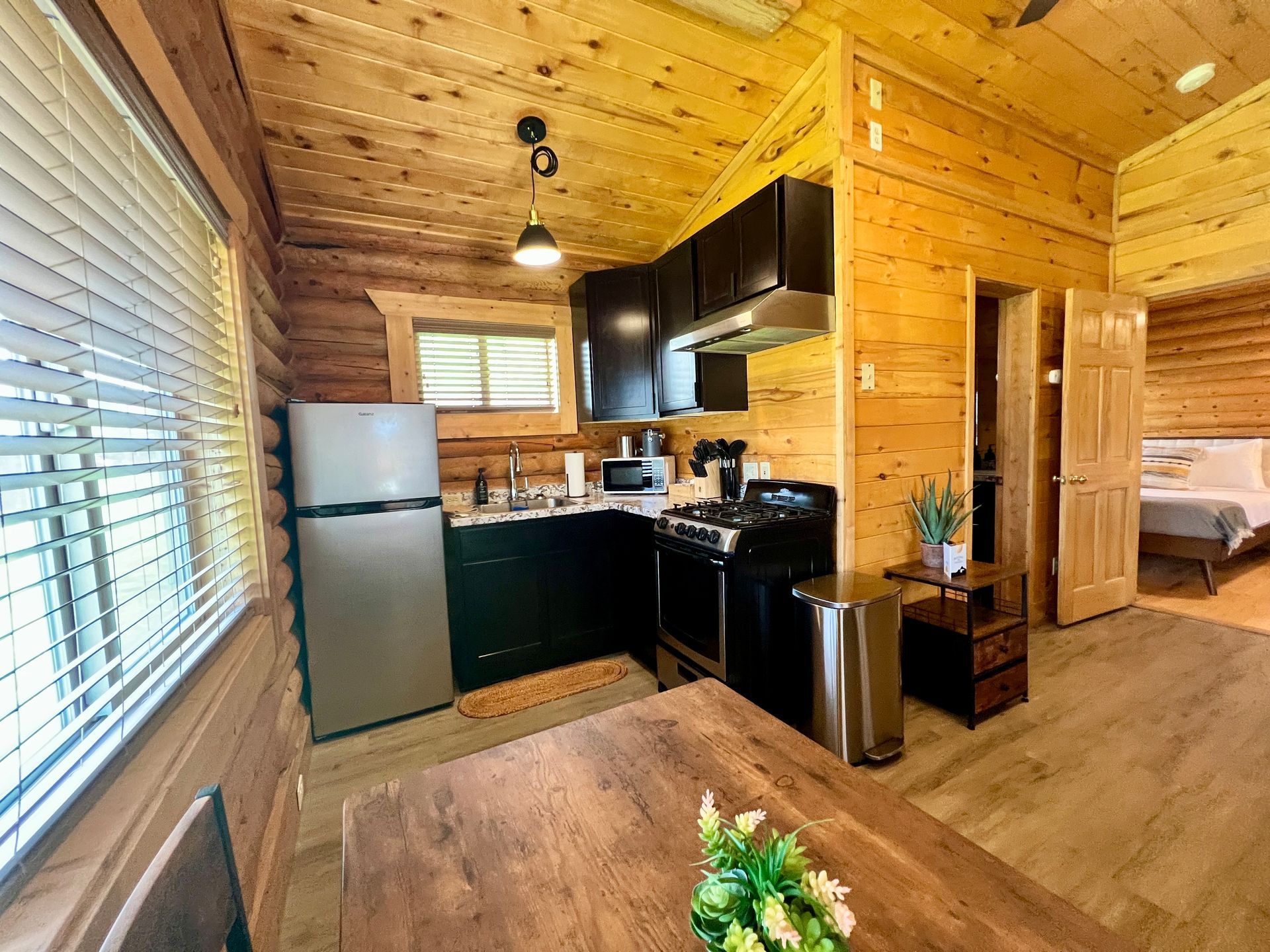 Small cabin interior with a kitchen, dining area, and bedroom, all with wood paneling.