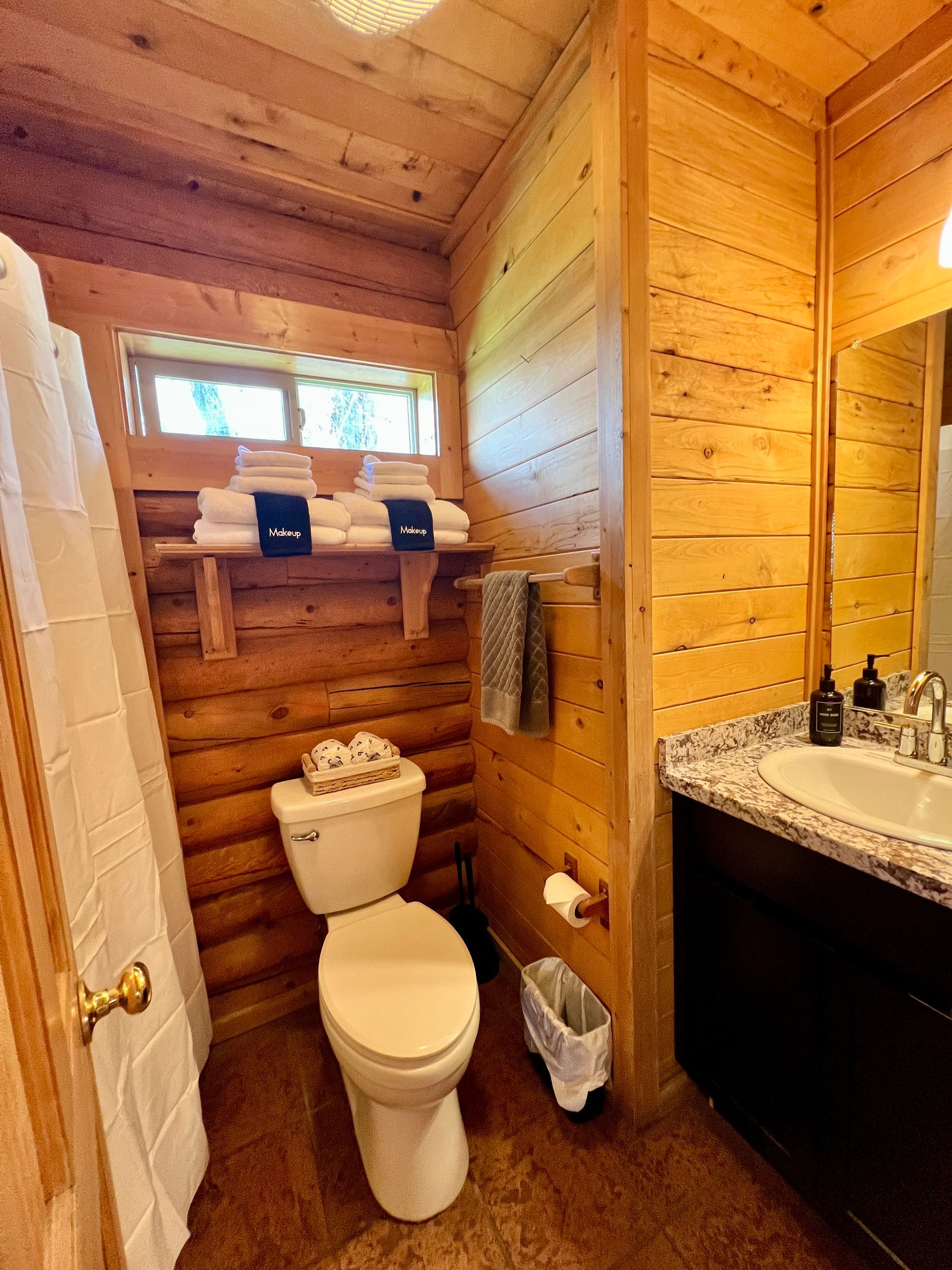 Bathroom with wood paneling, toilet, sink, and shower curtain.  Towels on a shelf.