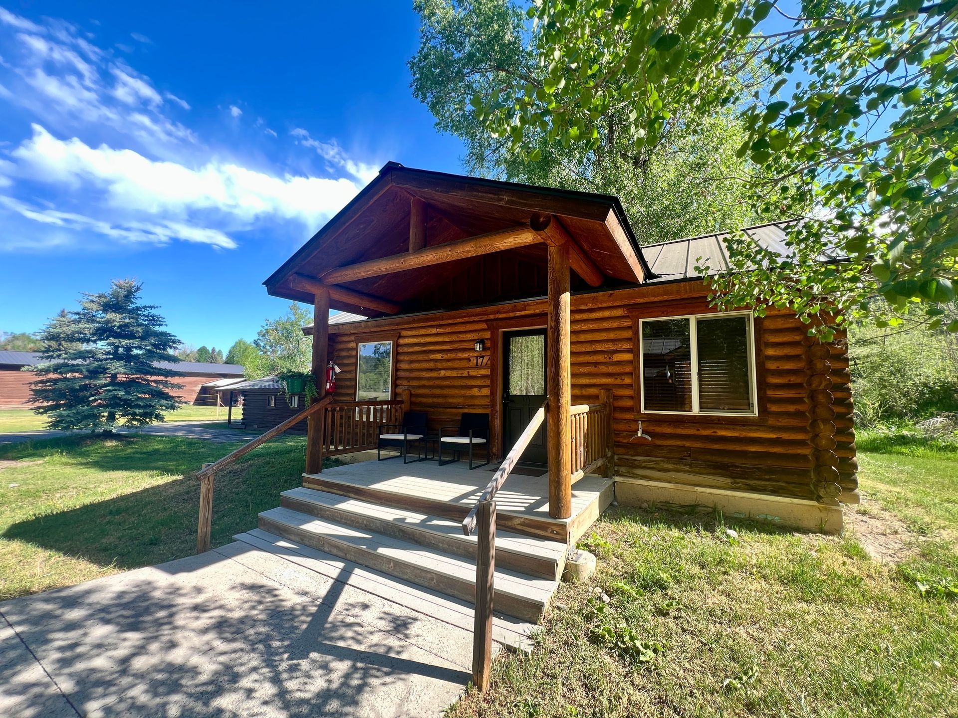 Log cabin with porch, concrete steps, set in grassy yard under blue sky.