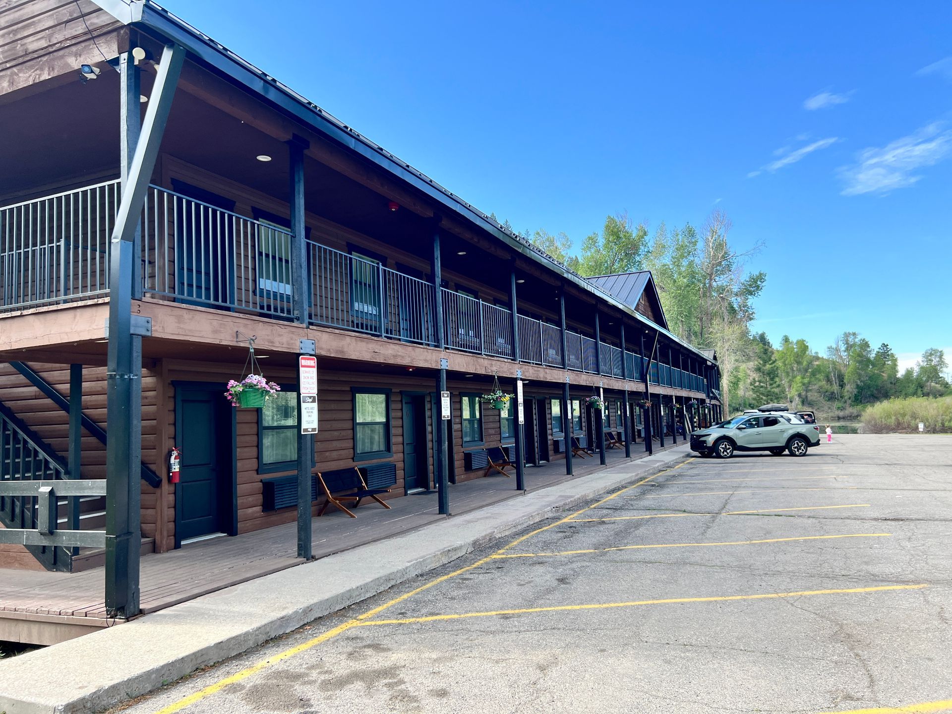 Log-cabin-style motel with a second-floor balcony. A car parked in front. Clear, sunny day.
