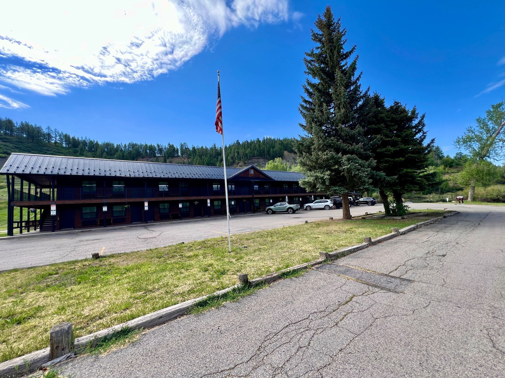 Lodge-style building with a flag on a sunny day, parked cars visible.