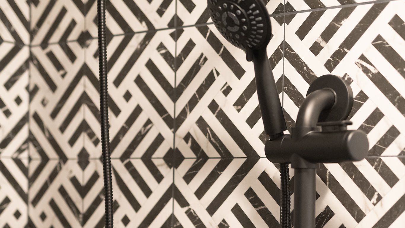 Black showerhead on a patterned black and white tile wall.