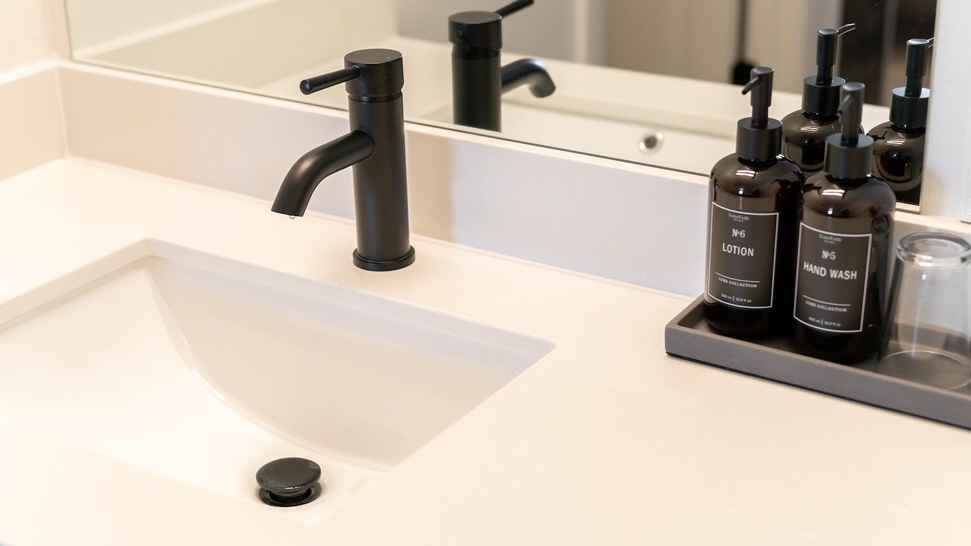 Black faucet and sink in a modern bathroom with toiletries and a mirror.