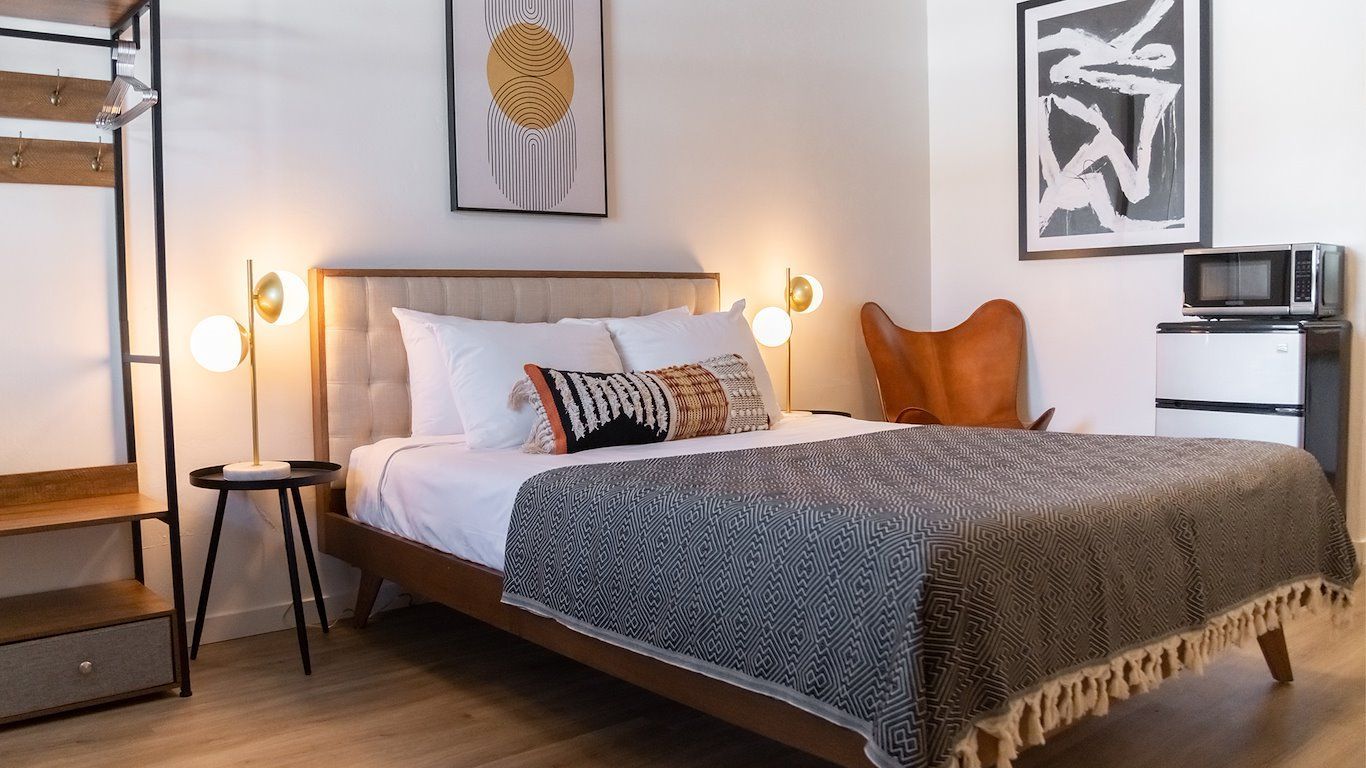 Bedroom with bed, art, armchair, and microwave. White walls, neutral tones.