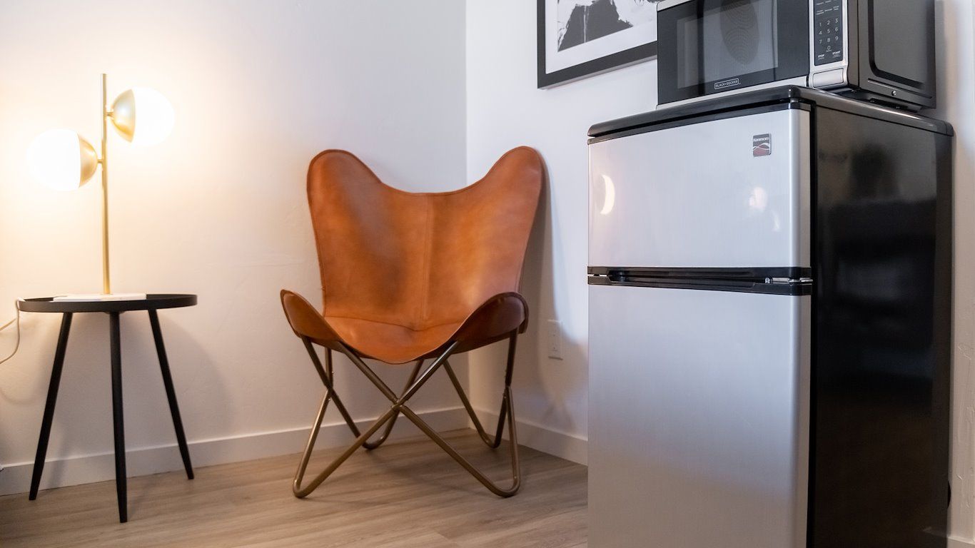 A small room with a leather butterfly chair, side table, fridge, and microwave.