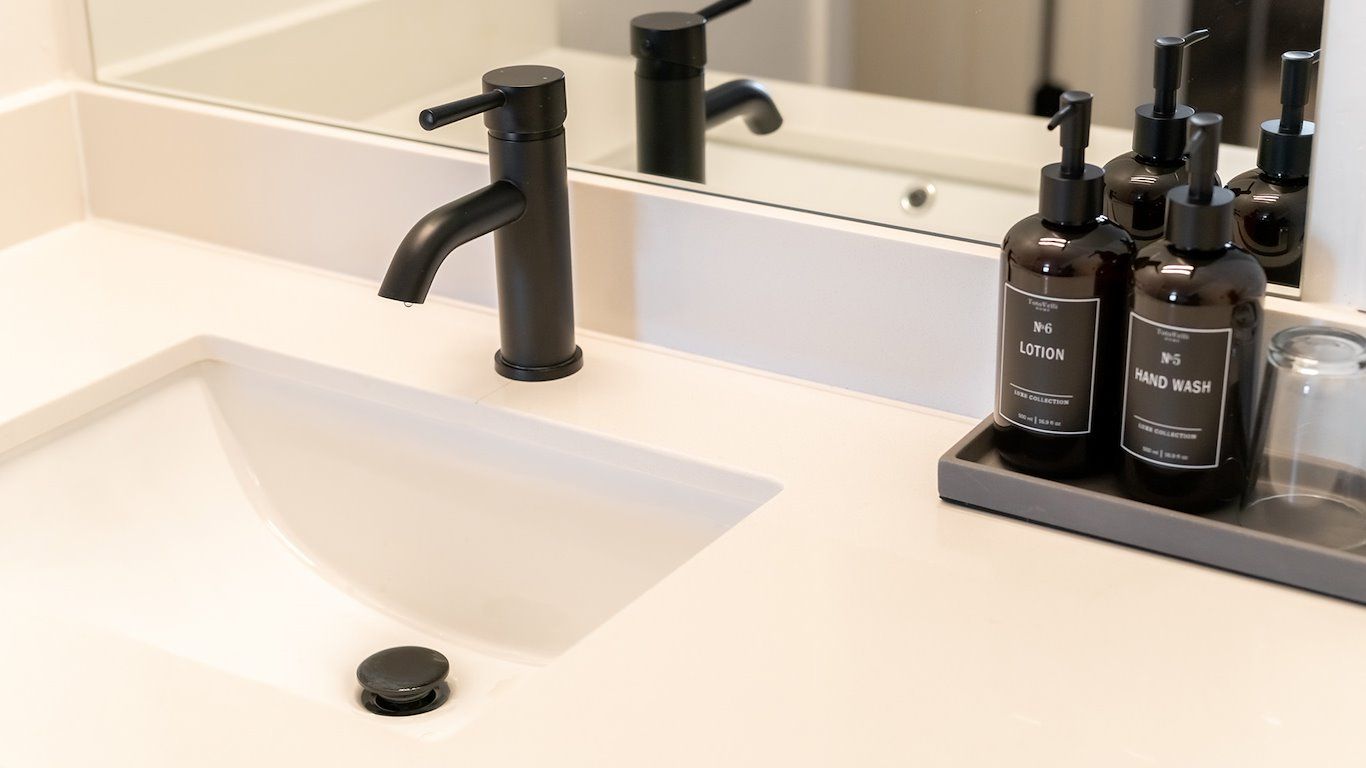 White bathroom sink with black faucet, brown soap bottles on the counter, and mirror.