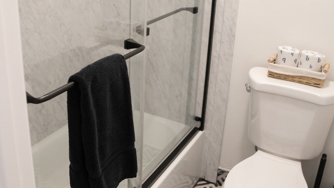 Black towel hangs on a shower door in a white bathroom with a toilet and decorative basket.