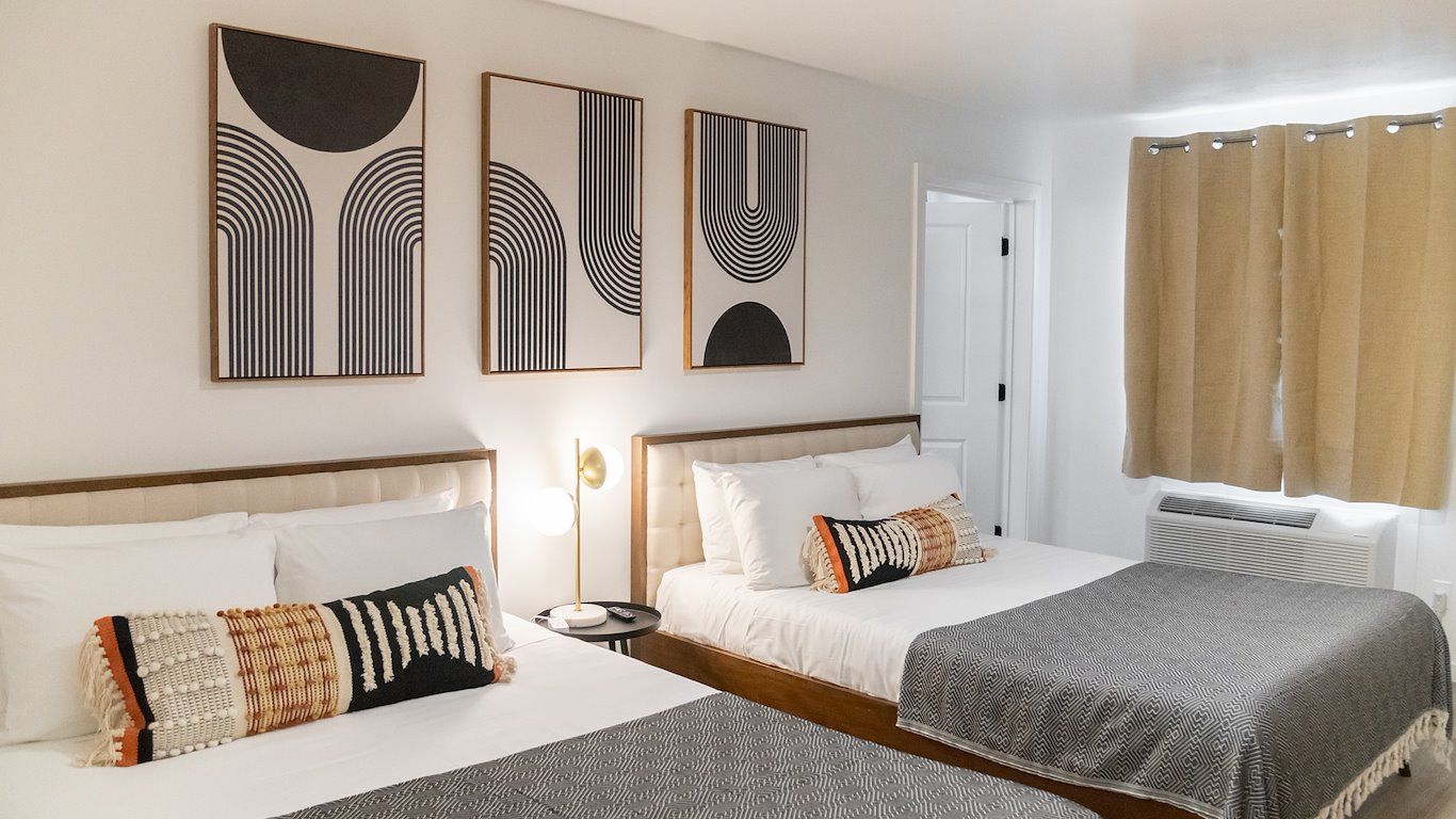 A hotel room with two queen beds, artwork, and a window with tan curtains.