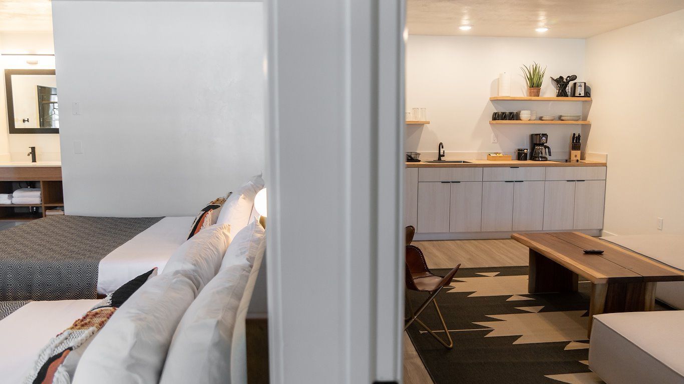A view through a doorway, showing a bedroom to the left and a kitchen with a seating area to the right.