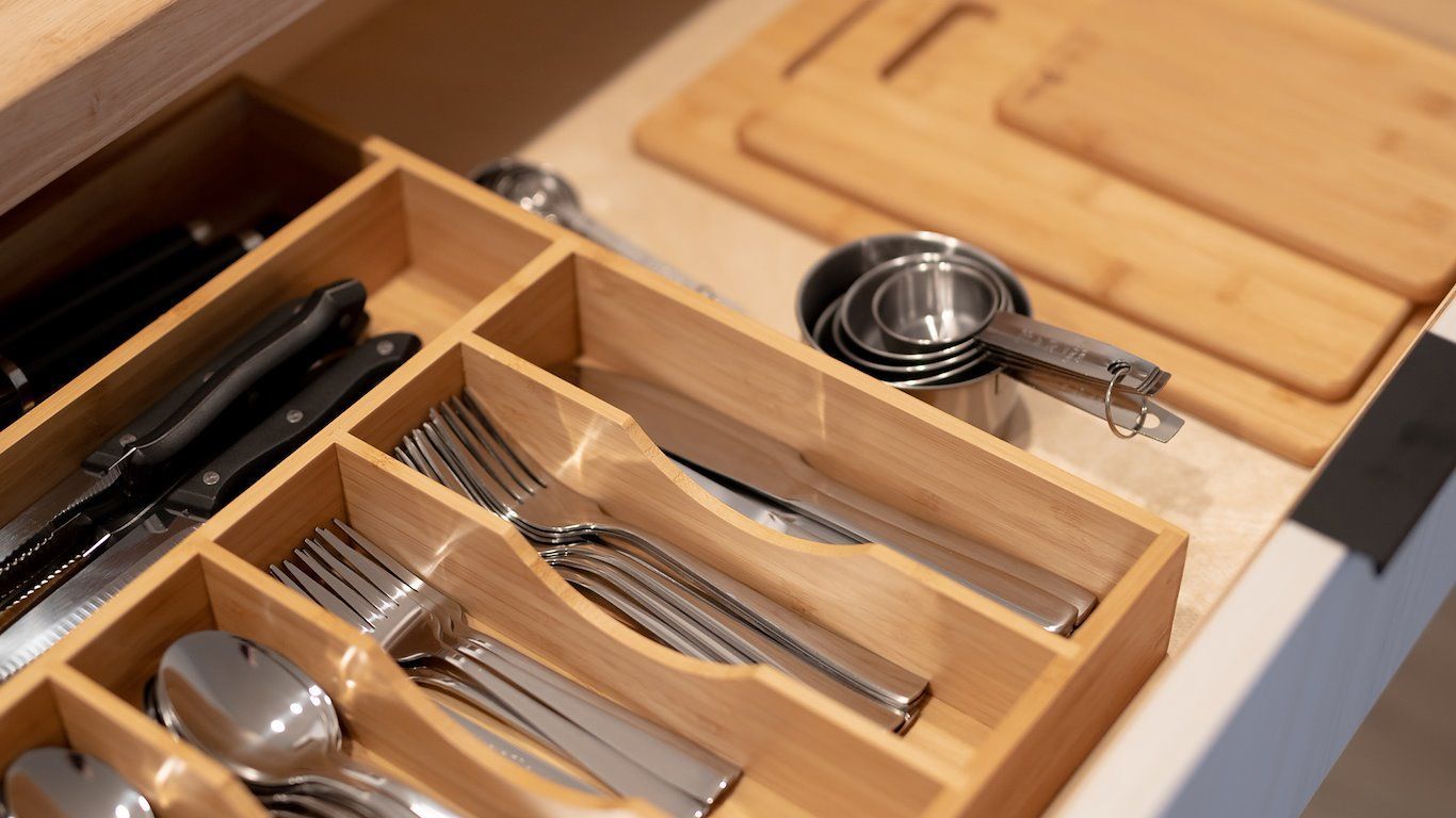Wooden kitchen drawer with cutlery and measuring cups, next to cutting boards.