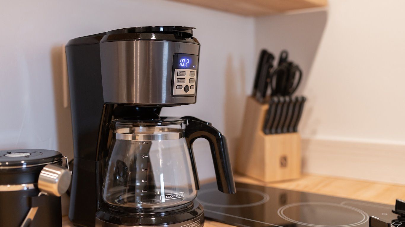 Black coffee maker and glass carafe on kitchen counter near knives.