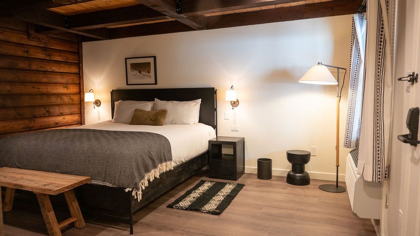 Bedroom with a bed, bench, and floor lamp. Log wall on the left.