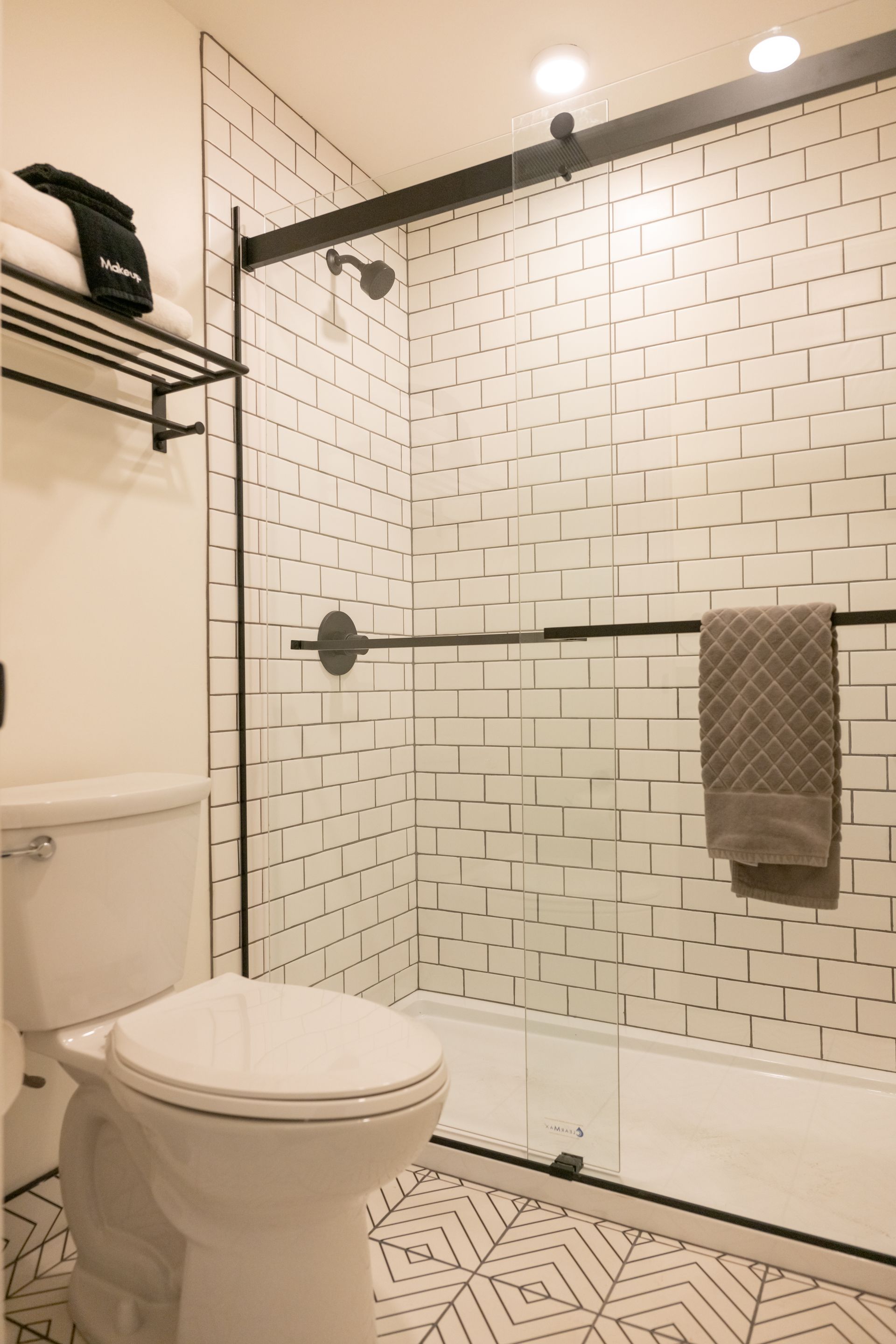 Modern bathroom with white subway tile, glass shower, black fixtures, and patterned floor.