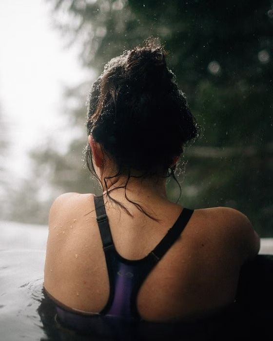 Woman in swimsuit in a pool, back to the camera, rain falling.
