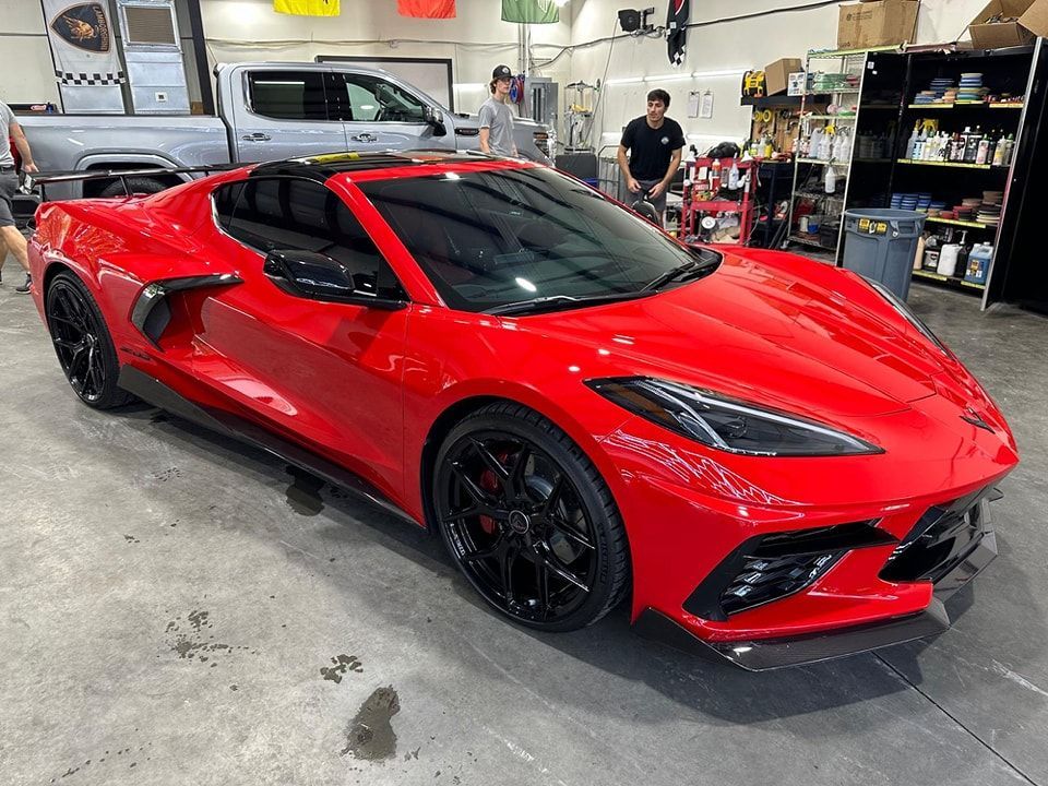 Red sports car with black wheels in a garage. Two people stand near the car.