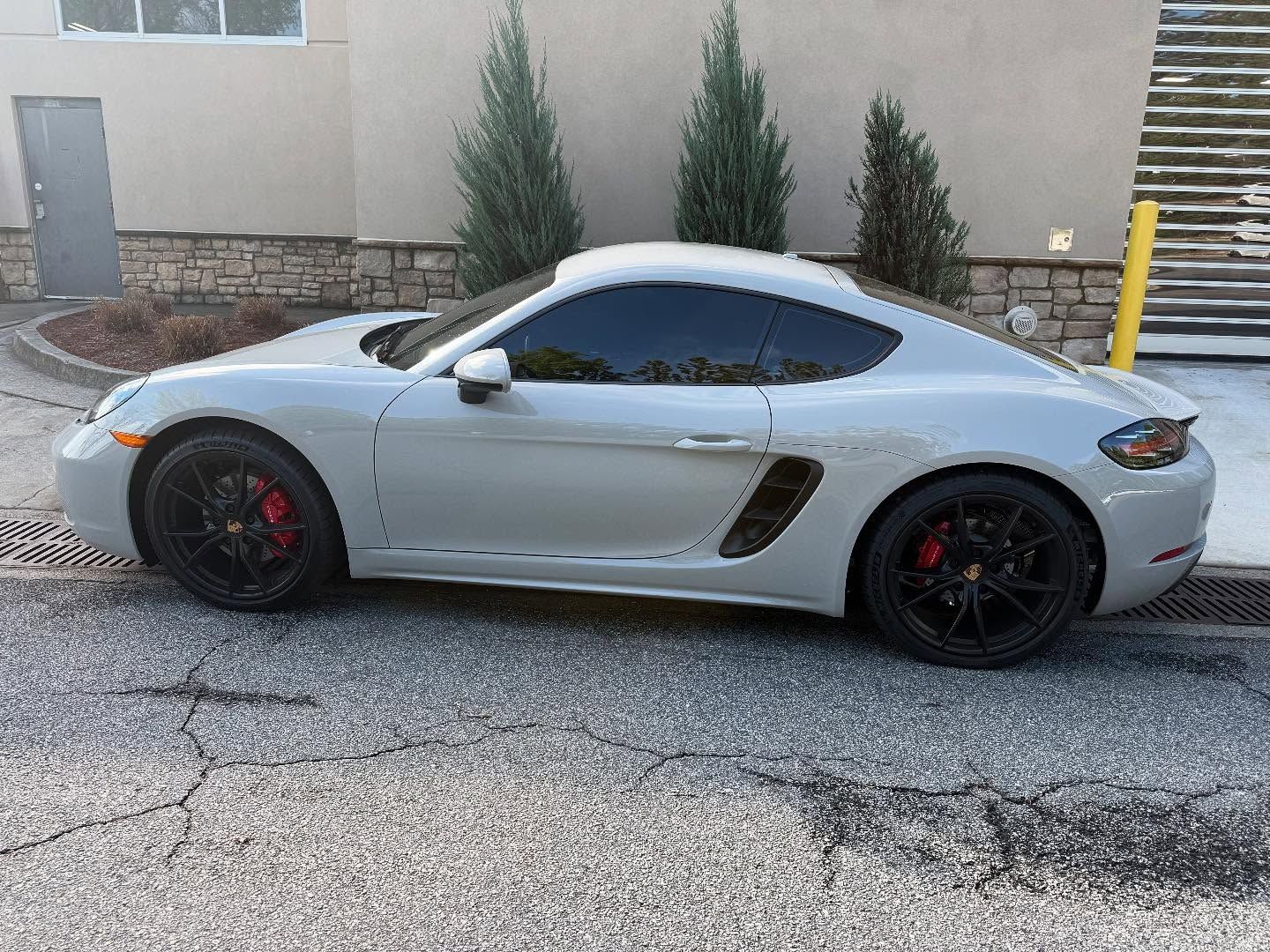 Gray Porsche sports car parked on asphalt, red brake calipers, tinted windows.